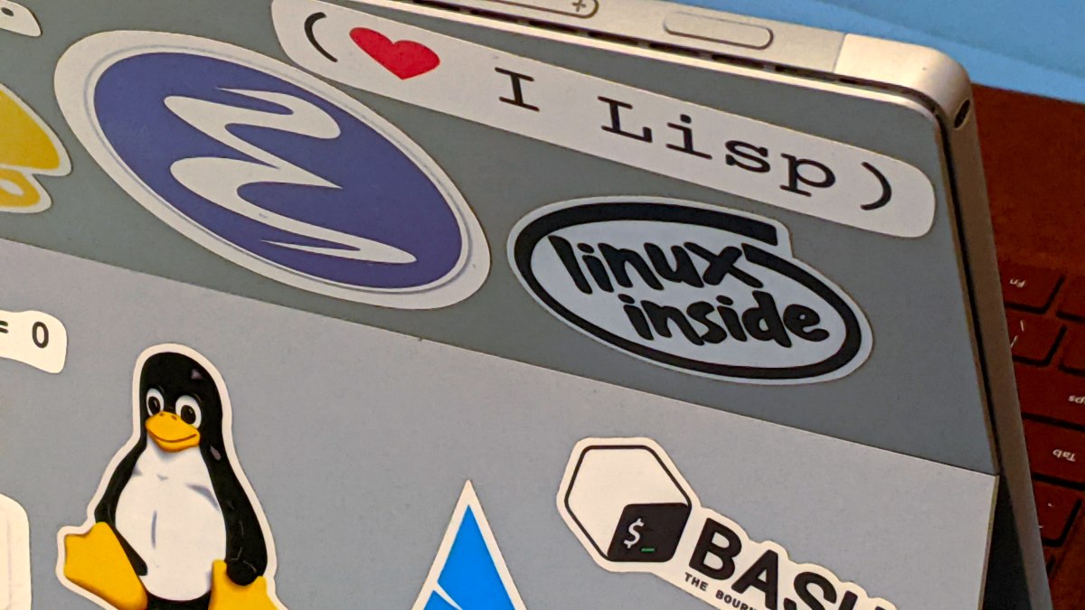 Cover image: Photo of the back of a 2-in-1 laptop with several stickers including Tux the penguin, the Emacs logo, one that says “linux inside” and another with a love heart followed by the words “I Lisp.”
